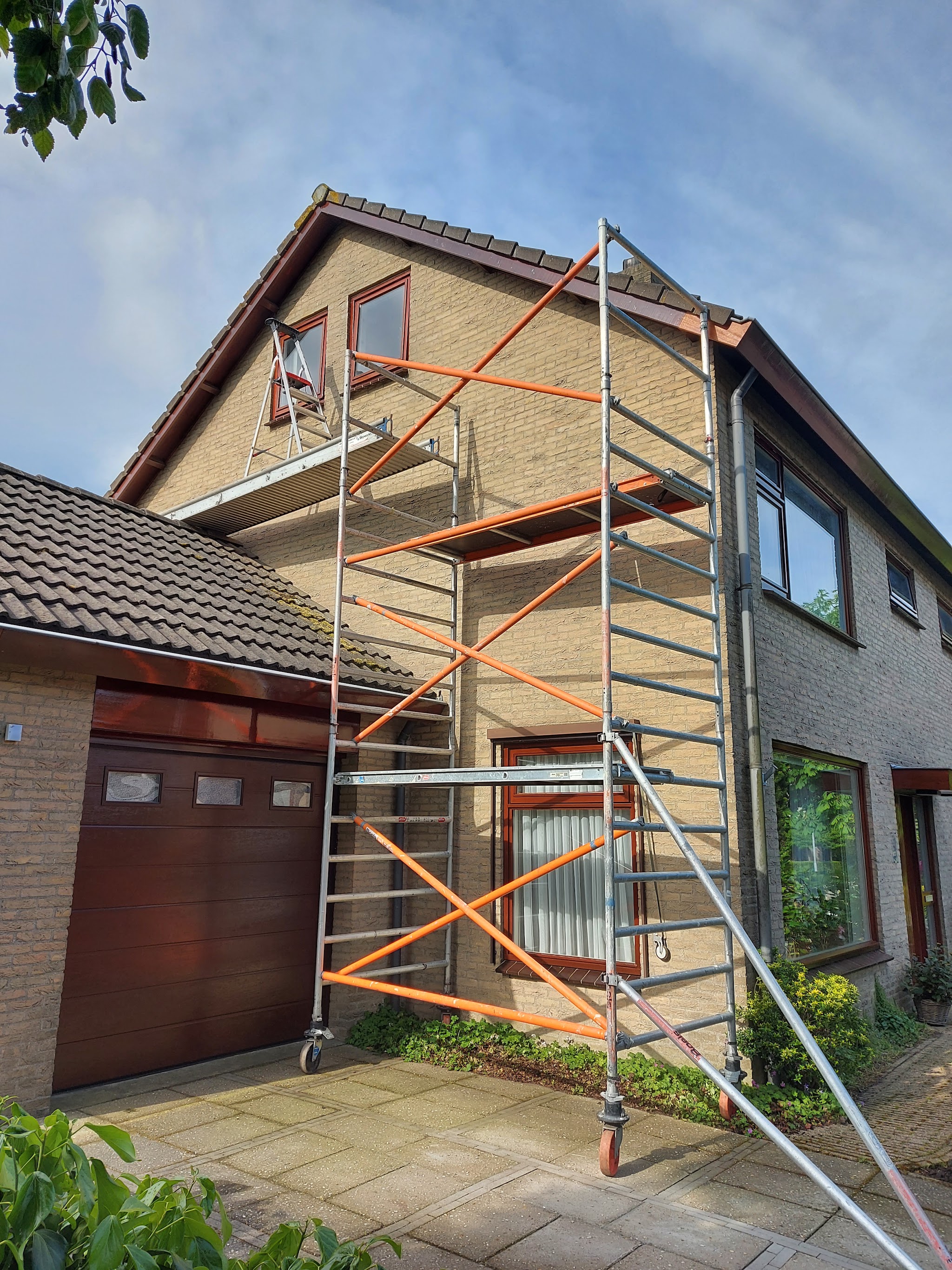Bakstenen woning met rolsteiger tot aan de topgevel, met donkerrode garagedeur en kozijnen