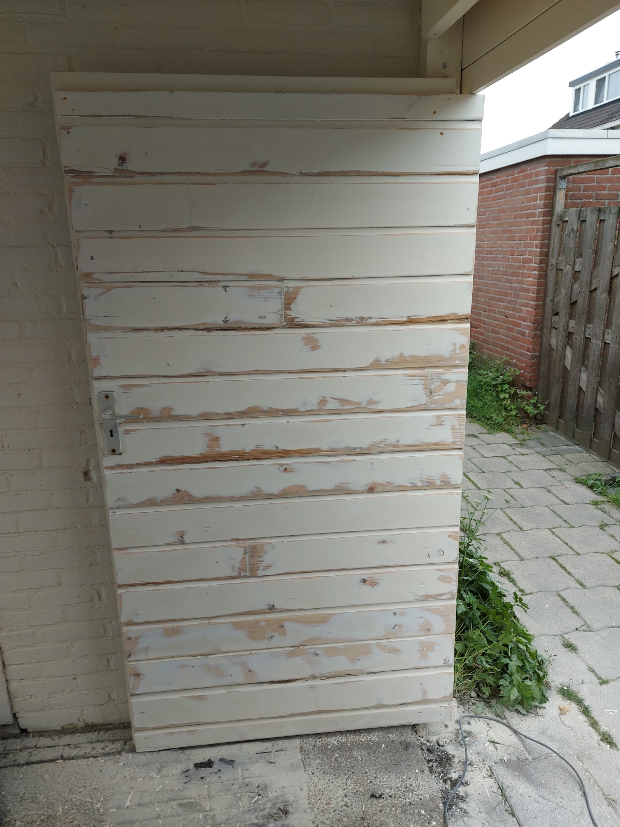Verweerde houten planken met afbladderende witte verf, vóór de schilderbeurt