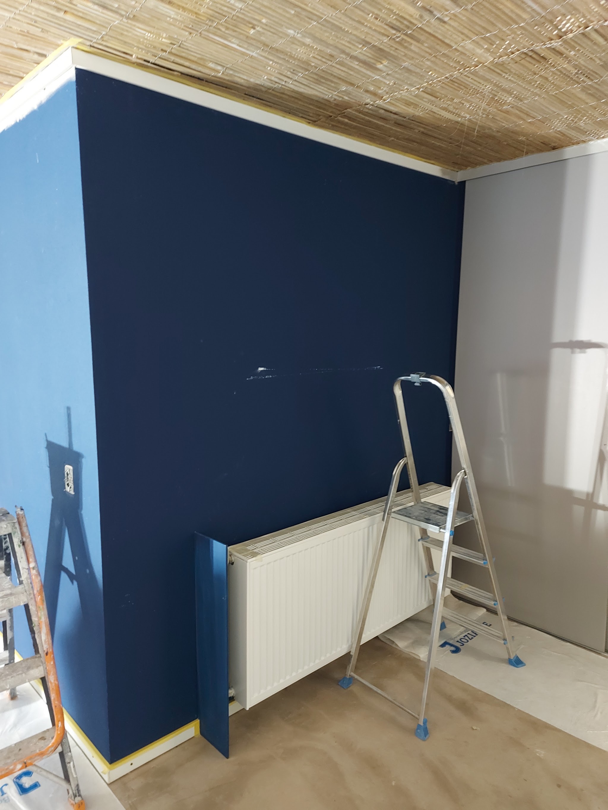Donkerblauw geschilderde accentwand met radiator en afgeplakte vloer